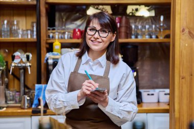 Woman working in restaurant cafe bar coffee shop bistro looking at camera with notepad. Small business, service, work, staff concept