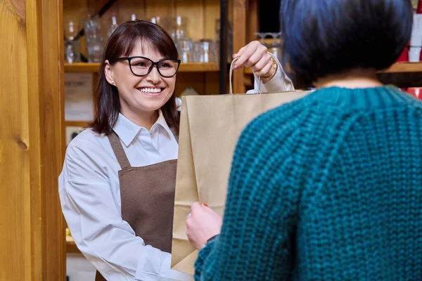 Woman restaurant worker issuing an order for takeaway food in paper bag. Internet orders, food delivery, food sale, small business, service work staff concept