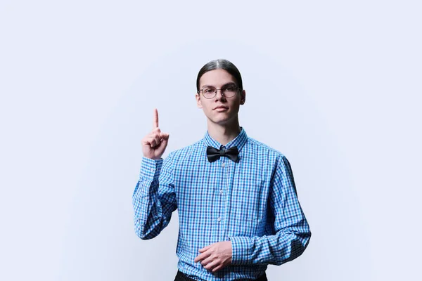 Serious confident guy student showing thumbs up, white background. Handsome teenage young male in glasses bow tie shirt looking at camera hand gesture attention announcement space for advertising text