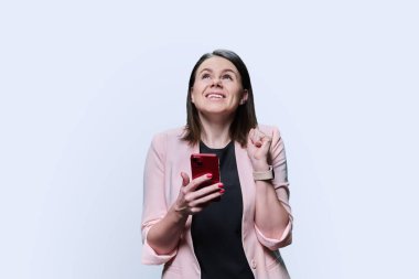 Dreamy thinking young woman with smartphone in her hands on white studio background