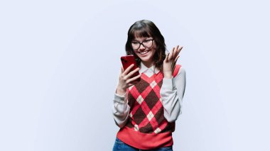 Surprised young female looking at smartphone screen on white studio background. Shocked excited girl reading text on phone. Emotions, lifestyle, youth concept