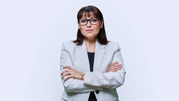 Middle aged businesswoman in glasses light suit with crossed arms on a white studio background. Confident positive 40s female looking at camera. Business lady, leader, manager, mature people concept