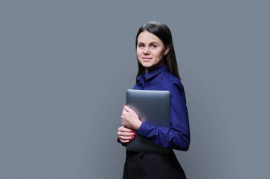 Portrait of smiling young business woman with laptop, confident female looking at camera on grey color background. 30s female manager banker teacher using pc for e-learning remote work online service