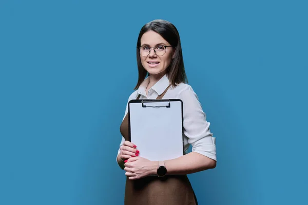 Young Positive Woman Apron Clipboard Posing Blue Studio Background Smiling — Stockfoto