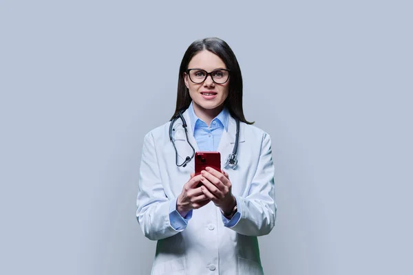 Giovane Medico Donna Guardando Fotocamera Utilizzando Smartphone Sfondo Grigio Chiaro — Foto Stock