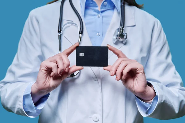 Close-up credit card in the hands of a doctor, on a blue studio background. Insurance, healthcare, medicine, credit card service concept