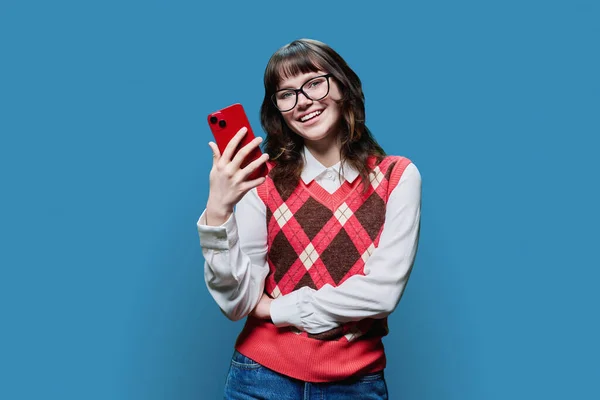 Sonriente Joven Hembra Con Teléfono Inteligente Fondo Del Estudio Azul — Foto de Stock