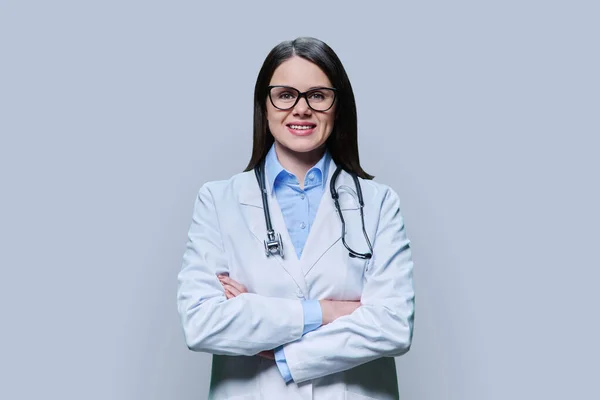 身穿白衣的积极自信女医生的画像 双手交叉 在浅灰的工作室背景上看着相机 医务人员 科学医学概念 — 图库照片