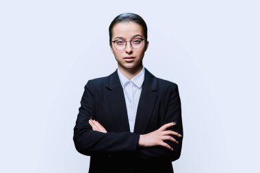 Siyah gözlüklü ciddi bir bayan öğrenci beyaz stüdyo arka planında kameraya bakıyor. Kollarını çapraz yapmış kendinden emin bir genç kız. Ergenlik dönemi lise yaşam tarzı eğitimi, gençleri eğitme
