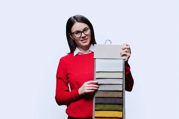 Young woman holding hanger with different colors of upholstery curtain fabric, on white background. Female client buyer designer decorator choosing textiles for interior, new home renovation design