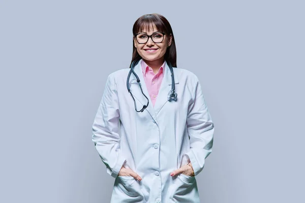 中年妇女医生的画像 白色外套 灰色工作室背景 正笑着看着成熟的医学女性镜头 医务人员 科学医学概念 — 图库照片