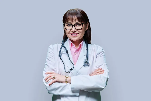 有自信的成熟女医生的画像 身穿白衣 双手交叉 背景灰暗 在镜头前微笑的中年女性 职业医学职业健康保护卫生保健 — 图库照片
