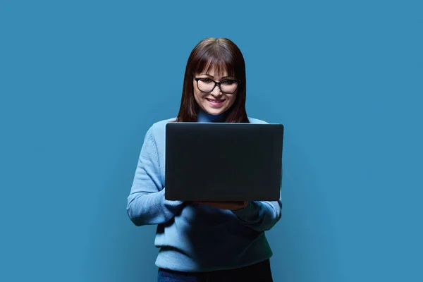 Friendly Mature Woman Using Laptop Blue Studio Background Smiling Middle — Stock Photo, Image