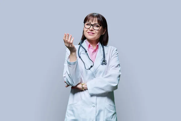 中年妇女医生的画像 白色外套 灰色工作室背景 正笑着看着成熟的医学女性镜头 医务人员 科学医学概念 — 图库照片