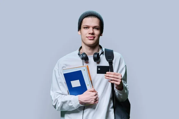 Portrait of college student guy with bank credit card, on gray studio background. Banking services for college, university, high school students, payment, shopping for goods and services