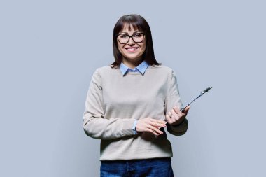 Açık gri arkaplan üzerine kağıt dökümanları olan orta yaşlı kadınların portresi. Kameraya bakıp gülümseyen olgun bir kadın. Satış Lojistiği İş Yönetimi Yönetim Personeli Öğretmenliği