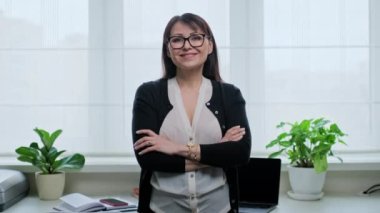 Ofiste kendinden emin olgun bir kadının portresi. Orta yaşlı kadın kameraya çapraz kollarla bakıyor. Serbest meslek, uzak iş, online öğretmen psikolog muhasebeci yasal, internet hizmeti