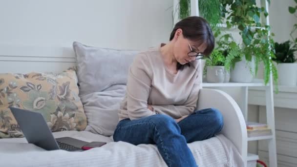 闷闷不乐的中年妇女坐在家里的沙发上 身体有问题 与年龄有关的荷尔蒙变化 工作困难 成熟年龄观念 — 图库视频影像