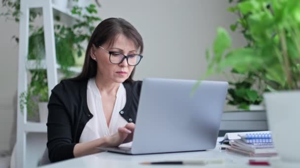 自宅のオフィスで働く深刻な中年の女性は 女性の机のラップトップに入力して座っている フリーランスリモートビジネスオンライン指導心理学者会計士法的 インターネットサービス — ストック動画