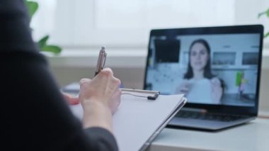 Çevrimiçi sanal toplantı, dizüstü bilgisayarda konuşan genç bir kadın ve not alan bir kadın. Çalışma, terapi, eğitim ve iş dünyasındaki video internet teknolojileri.