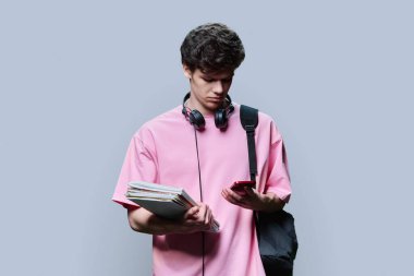 Sırt çantalı, kulaklıklı, ders kitaplı, gri stüdyo geçmişine bakan ciddi bir üniversite öğrencisi. Pembe tişörtlü yakışıklı genç, kıvırcık saçlı, eğitimli.