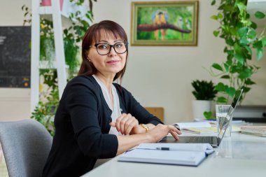 Ev ofisinde çalışan orta yaşlı bir kadının portresi. Masada dizüstü bilgisayar kullanan bir kadın. Serbest çalışan uzaktan kumandalı internet öğretmenliği psikolog muhasebecilik hukuk danışmanı, İnternet