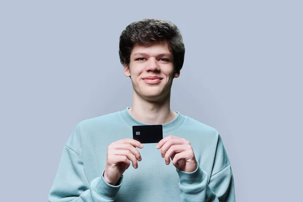 Młody Przystojniak Trzymający Rękach Kartę Kredytową Szarym Tle Studia Uśmiechnięty — Zdjęcie stockowe
