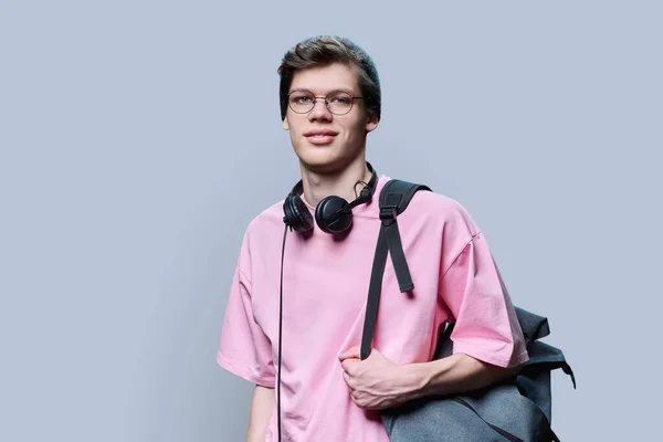穿着粉色T恤 背景为灰色的时髦年轻男性嬉皮士 戴着针织帽子眼镜 头戴耳机背囊 看着相机的帅哥 生活方式 20岁青年 — 图库照片