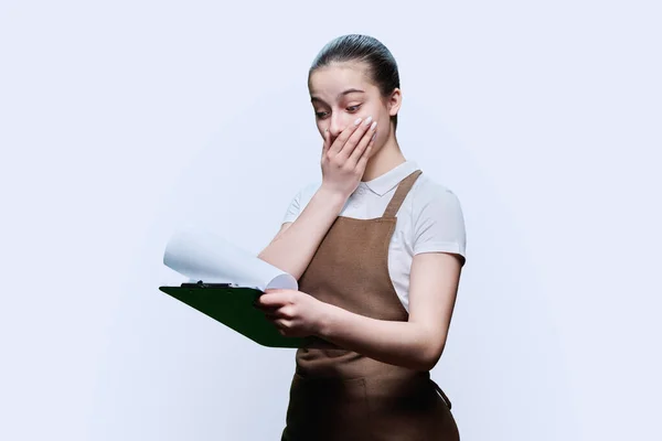 穿着围裙的年轻女服务员看到有白色工作室背景的剪贴板时 大吃一惊 服务部门的工作 学生就业 咖啡店的工作人员 — 图库照片