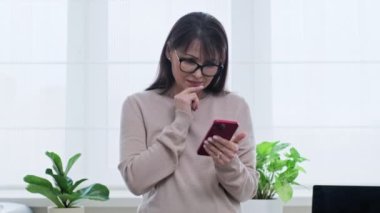 Akıllı telefon kullanan olgun bir kadın, ekrana bakıyor, geziniyor, dinleniyor, boş zaman teknolojisi orta yaşlı insanlar kavramı