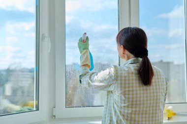 Evdeki pencereleri sprey ve mikrofiber bez kullanarak temizleyen kadın. Ev temizliği, ev işi, temizlik, iş, hizmet kavramı