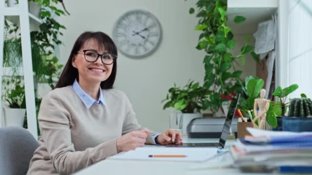一个面带微笑的中年女性坐在办公室工作时看着相机的画像 远程工作和服务 自由职业 成年人就业 — 图库视频影像