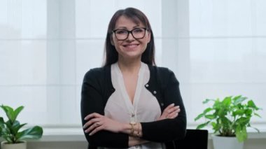Ofiste kendinden emin olgun bir kadının portresi. Orta yaşlı kadın kameraya çapraz kollarla bakıyor. Serbest meslek, uzak iş, online öğretmen psikolog muhasebeci yasal, internet hizmeti