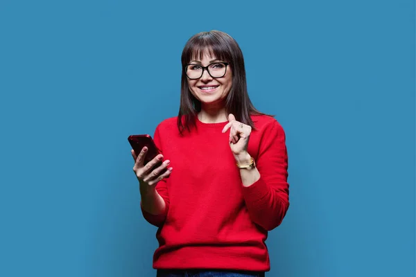 Glad Medelålders Kvinna Med Smartphone Bär Röd Jumper Tittar Kameran — Stockfoto