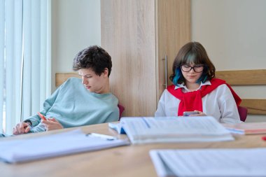 Ergen öğrenciler sınıfta bir molada oturup akıllı telefonlar kullanarak dinleniyorlar. Ergenlik, yaşam tarzı, eğitim, eğlence teknolojisi, gençlik konsepti