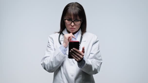Kobieta Średnim Wieku Lekarz Pomocą Smartfona Szarym Tle Lekarka Białym — Wideo stockowe