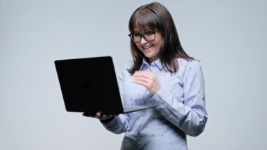 Orta yaşlı mutlu iş kadını, gri arka planda el ele tutuşan dizüstü bilgisayar okuyor. İş, iş, iş, hizmet ve internet teknolojisi için laptop kullanan gözlüklü neşeli olgun bir kadın.