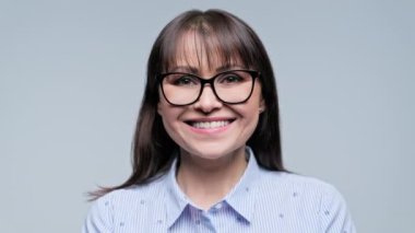 Gri arka planda kameraya bakan çekici, orta yaşlı bir kadının yakından çekilmiş yüzü. Güzellik sağlığı, 40 'lı yaşlar, moda gözlüklü kadınlar, diş tebessümü, diş implantı görme optiği konsepti.