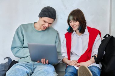 Dost yeniyetmeler, genç erkekler ve kız sırt çantalarıyla yerde oturuyor ve çalışma odasının koridorundaki ekrana bakıyorlar. Moda gençliği, yaşam tarzı, iletişim, arkadaşlık kavramı