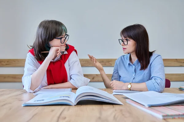 Young teenage female studying foreign languages in course with teacher. Tutor and student sitting at desk in office, using books, notebooks. Education, knowledge, learning concept