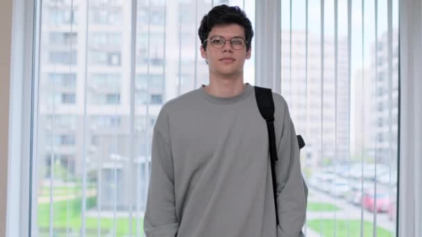 一个大学生在教室的橱窗里看着相机的画像 19岁的年轻男性戴着眼镜 背负着背包在教育中心摆姿势 — 图库视频影像