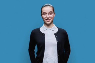 Mavi stüdyo geçmişinde mutlu lise öğrencisinin portresi. Dişleriyle gülümseyen, gözlüklü genç bir kadın kameraya bakıyor. Ergenlik, yaşam tarzı eğitimi boş zamanlardaki gençler.