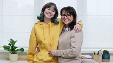 Mutlu orta yaşlı anne-kız 18 yaşında, 19 yaşında pencerenin yanında kameraya bakarak gülümsüyor. Aile içi ilişkiler, ebeveyn desteği, arkadaşlık kavramı