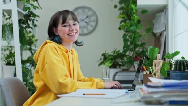 10代の女性がノートパソコンを持って自宅の机に座ってカメラを見て笑っている 若い流行の女の子18 19歳 大学生 正の肖像画 ライフスタイル 勉強レジャーコミュニケーション — ストック動画