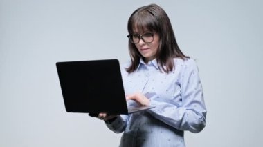Orta yaşlı ciddi iş kadını. Gri arka planda el ele tutuşan dizüstü bilgisayar okuyor. İş, iş, iş, hizmet ve internet teknolojisi için dizüstü bilgisayar kullanan yetişkin bir kadın.
