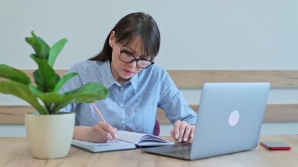 中年妇女与笔记本电脑一起工作 坐在办公桌前 做笔记 工作自信 成熟的人的概念 — 图库视频影像