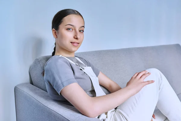 一个沉着微笑的少女坐在家里沙发上的画像 看着镜头 年轻的女性感到很不舒服 青春期 16岁青少年 生活方式概念 — 图库照片