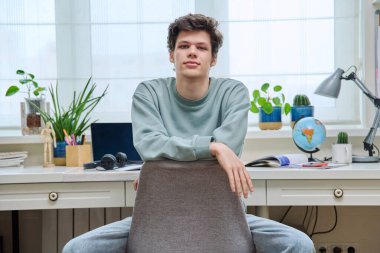 Evin içinde pencerenin yanında oturan yakışıklı genç adam. Gülümseyen mutlu erkek kameraya bakıyor. Yaşam tarzı, gençlik kavramı