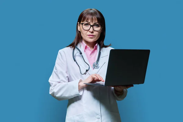 Mature Female Doctor Using Laptop Computer Blue Studio Background Confident — Stock Photo, Image