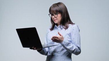 Orta yaşlı iş kadını elinde dizüstü bilgisayarla görüntülü konuşma konferansı yapıyor, web kamerasından gri arka planda konuşuyor. Çevrimiçi uzaktan hizmet, iş, iş, iş, internet teknolojisi